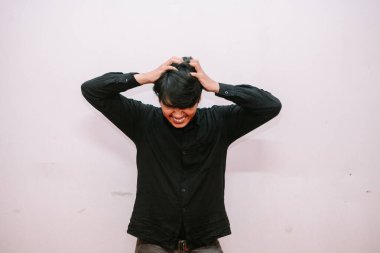 Stresli ve hayal kırıklığına uğramış genç bir adam saçını çekiyor. Umutsuzluğu ve beyaz bir arka plana karşı ezilmeyi gösterir..