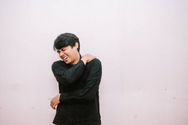 Istırap içindeki genç adam omzunu tutuyor, rahatsızlık gösteriyor. Düz arkaplan ile çekim.