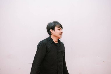 Düz soluk bir arka planda siyah gömlekli dalgın Asyalı bir adamın portresi. Düşünceli bir ifadesi var..