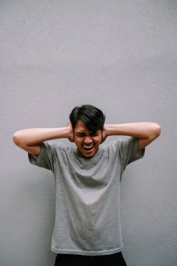 Genç bir adam kulaklarını korkunç bir sesten koruyor. Stres ve endişe ifadesi sergiliyor.