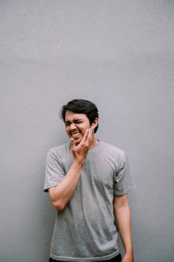 Korkunç bir diş ağrısı çeken genç bir adam, acı ve rahatsızlık içinde yüzünü tutuyor. Dişlerinde sorun olduğunu gösteren ifade.