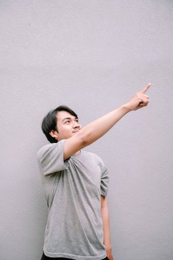 Asyalı bir adam kendinden emin bir şekilde yukarıya bakıyor. Gri arkaplanda pozitif bir ifadeyle bir şey gösterme ya da gösterme