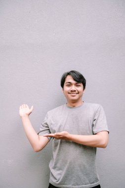 Genç adam gülümsüyor, sunuyor ya da tarafsız gri bir arkaplanı olan bir şey gösteriyor..