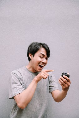 Hevesli bir adam merceğe işaret ederek başarıyı gösterir. Gri desenli arka planda izole edilmiş.