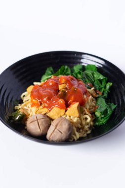 Köfteli, yeşil sebzeli ve canlı kırmızı soslu şehriye. Beyaz arka planda siyah bir kasede sunuldu..