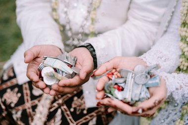 Mutlu bir gelin ve damat, geleneksel bir Cava düğününde zenginliğin ve kutsanmışlığın sembolü olarak ellerine para tutuşturur.