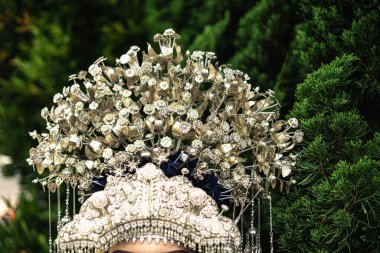 Üzerinde çiçek ve yaprak detayları olan gümüş bir başlık yakın plan, doğal yeşil arka plan ile ayarlanmış. Başlıkta karmaşık tasarımlar ve zarif süslemeler var..