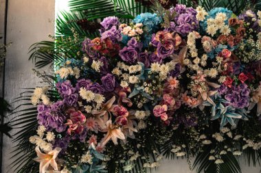 Güller, orkideler, zambaklar ve tropik yapraklar içeren gür ve canlı bir çiçek aranjmanı. Düğünler, etkinlikler veya zarif arka planlar için mükemmel..