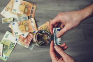 Erkek elleri kavanoza para koyuyor.