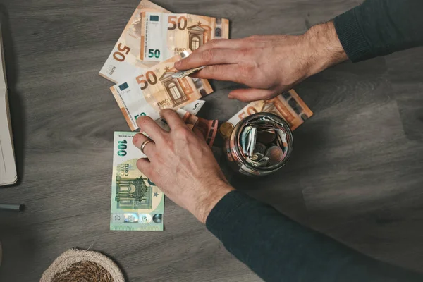 Erkek elleri kavanoza para koyuyor.