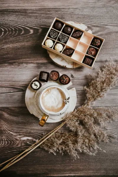 Sıcak beyaz kahve ve koyu ahşap arka planda küçük çikolatalı şekerler.