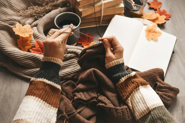 Woman hands knitting woolen sweater, working space indoors, coffee and vintage stuff around
