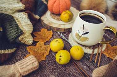 Sonbahar yapraklı bir fincan kahve ve ahşap arka planda örülmüş eşarp.
