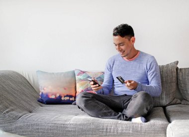 Uzaktan kumandalı ve akıllı telefonlu gülümseyen adam - mobil alışveriş, ödeme, ikinci ekran
