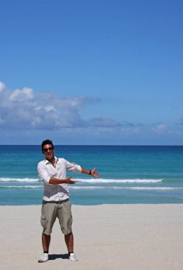 Bronz tenli ve güneş gözlüklü genç adam sahilin fotokopi alanında bir şey gösteriyor..