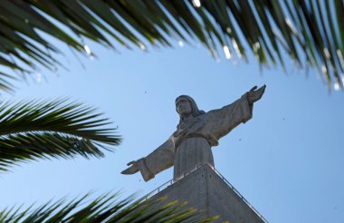 Cristo Rei - Portekiz, Almada 'daki İsa heykeli, bir palmiye ağacının yaprakları arasından görülüyor.