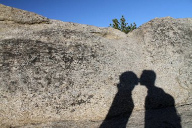 Yosemite Ulusal Parkı 'nda bir kayanın üzerinde öpüşen genç bir çiftin gölgesi.