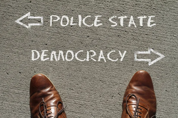 Top view on a man standing in front of the words Police State and Democracy with arrows pointing to the left and right side of the picture