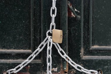 Metal asma kilit eski ahşap bir kapıya zincir takıyor.