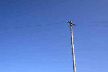 Mavi gökyüzünün önündeki elektrik hattı ve tahta direk.