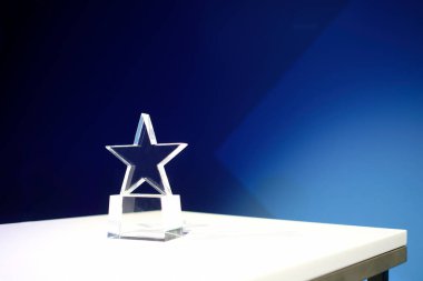 Üzerinde spot ışığı olan beyaz bir masanın üzerindeki camdan yapılmış yıldız şeklindeki ödül.