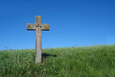 Arka planda mavi gökyüzü olan yeşil bir çimenlikte taştan yapılmış haç.