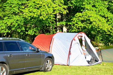 Ağaçların yanındaki arabanın yanındaki kırmızı-gri çadır. Hafta sonu kampı
