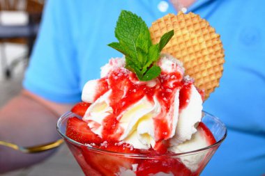 Nane yaprakları dondurmayı bardakta çilek reçeli ile süsler. Bir adam bir kafede dondurma yiyecek..