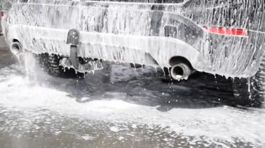 Otomobil yıkamada araba yıkayan biri. Köpük arabadan asfalta akar.