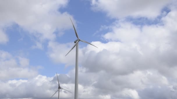 Kahden Tuuliturbiinin Valkoiset Terät Pyörivät Sinistä Taivasta Vasten Pilvillä — kuvapankkivideo