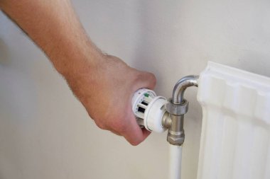Bir adam ısıtma radyatörünün sıcaklık topuzunu tutar. Isıtma hizmetleri, artan elektrik fiyatları