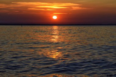 Gölde gün batımı. Suyun yüzeyinde güneş ışınlarının oynadığı küçük dalgalar var. Suyun üzerindeki güneş ışınlarından parlayan bir yol..