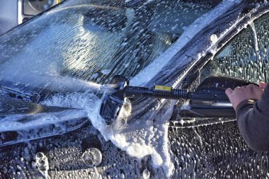 Bir adam oto yıkamada araba yıkar.