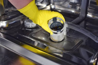 Kadın kirli filtreyi bulaşık makinesinden çıkarıyor. Manuel filtre temizliği, mutfaktaki ev aletlerinin bakımı..