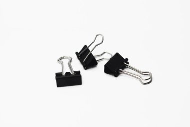 Beyaz arkaplanda izole edilmiş siyah ataçlar. Düzenli olması için kağıt yığınını klemplemek için kullanılan bir araçName