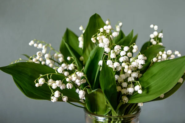 Stock image beautiful bouquet of Lilies of the valley, green and lilac flowers on a gray wooden background.