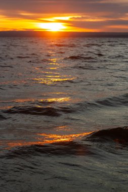 Gün batımını birkaç dalgayla birlikte bir su kütlesinin üzerinde..