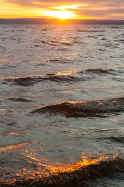Gün batımını birkaç dalgayla birlikte bir su kütlesinin üzerinde..