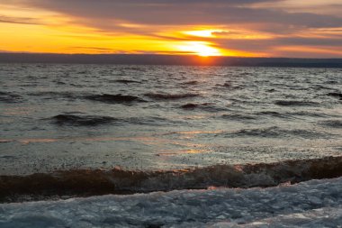 Gün batımını birkaç dalgayla birlikte bir su kütlesinin üzerinde..