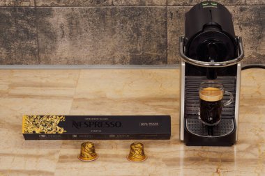Selanik, Yunanistan - 17 Aralık 2022: Otomatik Nespresso Orijinal espresso makinesi alüminyum kapsüllü. DeLonghi kahve makinesi ve bir fincan sıcak damlayan kahve ile metal Venezia kapsülleri..