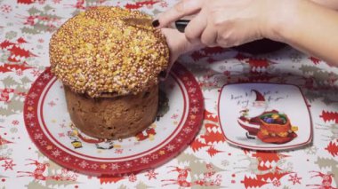 Geleneksel bir Noel panettone pastasını bıçakla kesen ve sofraya süslenmiş bir dilim koyan bir kadının üst görüntüsü..