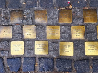 Selanik, Yunanistan - 24 Aralık 2022: 1943 'te Auschwitz' te öldürülen öğrencilerin isimlerinin bulunduğu bir lisenin önündeki Yahudi Stolpersteine Anıtı 'nın tepeden tırnağa sokak manzarası.