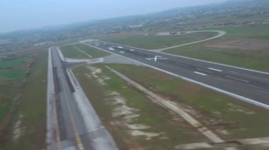 Lift off above runway under hazy weather looking to the right of the frame. Passenger window view aboard airplane cruising at low altitude above terrain in SKG airport Thessaloniki, Greece.