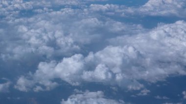 Travel flying above bed of puffy clouds, looking to the left of the frame. Passenger window view aboard an airplane cruising at high altitude.