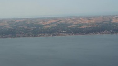 Low flying above terrain and coastline in Greece. Landscape aircraft passenger window view of settlements with low-rise buildings by the sea.