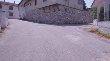 POV, Yunanistan 'da kırmızı kiremitli eski Balkan mimari tarzı evleri çevreleyen boş bir köy caddesine yürüyor.