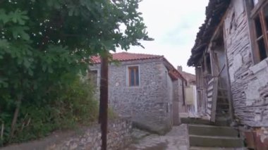 Day POV walking to an empty cobblestone alley around old low-rise stone-built houses with red tiles at Prespes lake area, Greece.