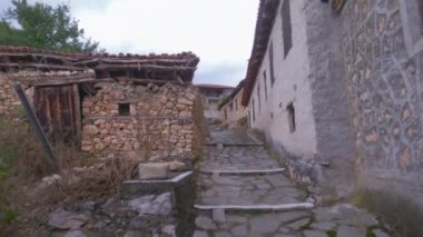 Day POV walking up to an empty cobblestone alley around old low-rise stone-built houses with red tiles at Prespes lake area, Greece.
