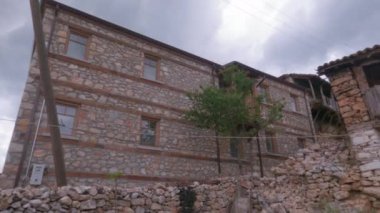 Day pan to an old low-rise stone-built damaged house with red tiles at Prespes lake area, Greece.