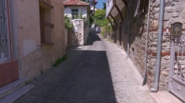 Day POV walking to an empty cobblestone alley around old low-rise stone-built traditional houses with red tiles at Xanthi, Greece.